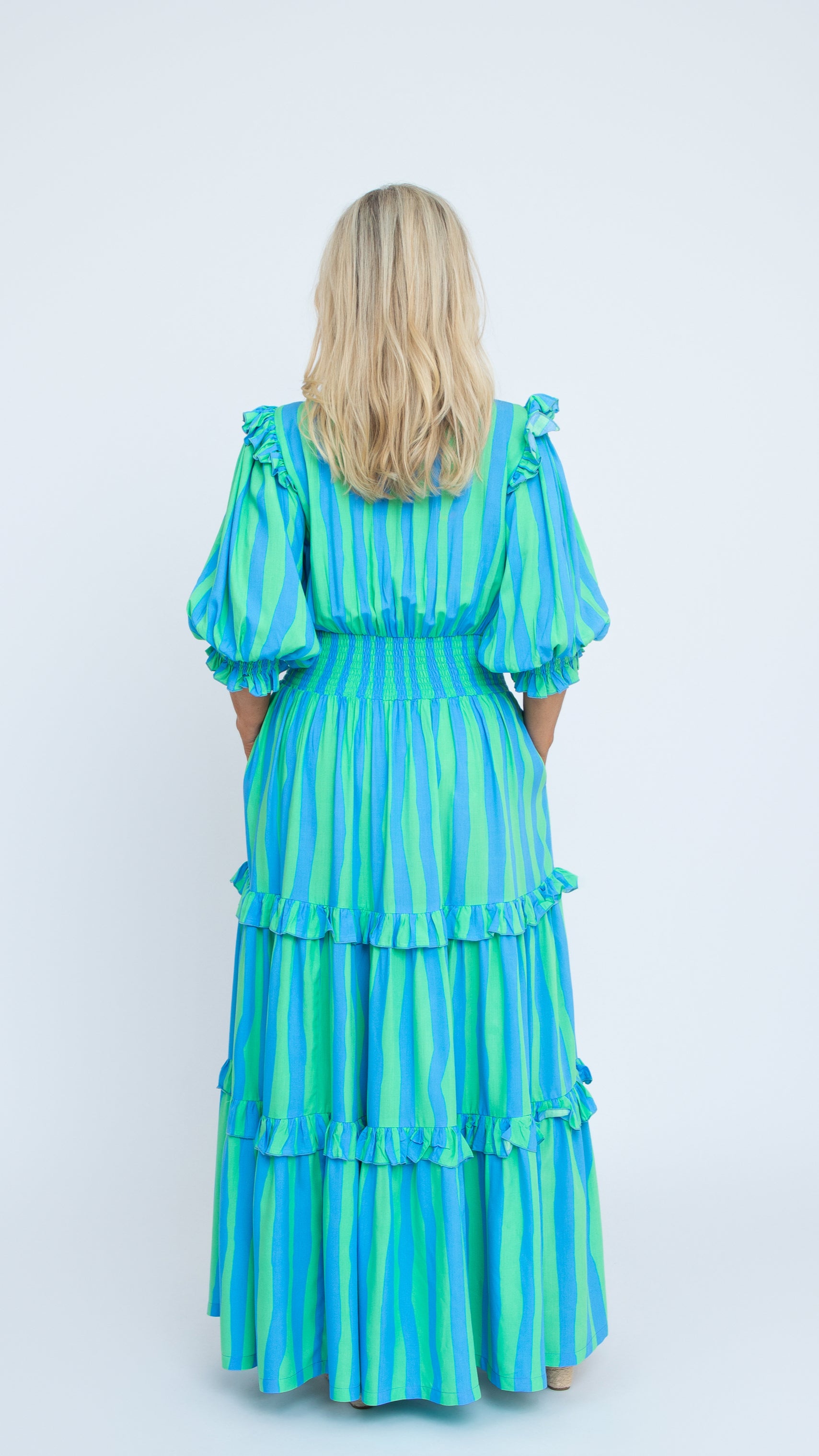 The Amy Dress in blue and green striped rayon with V-neck and puff sleeves, full-length tiered skirt. By Nancy The Label. Back view.