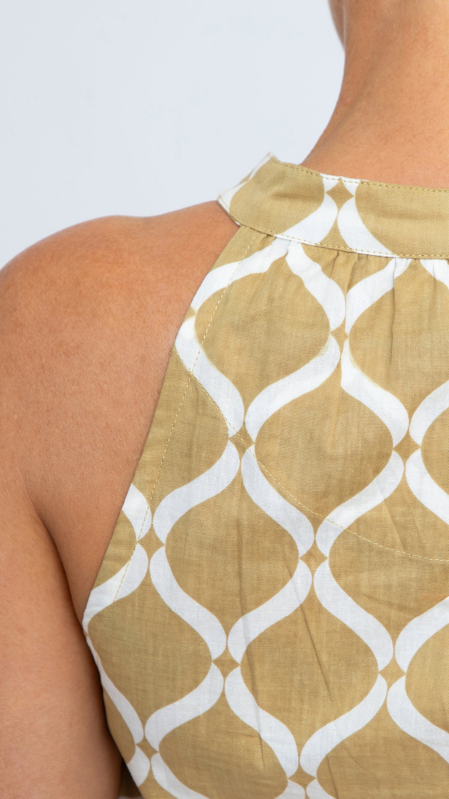 Close up of Donna Dress by Nancy The Label. Close-up of back neckline detail. Geometric Gold Trellis Print in Cotton. Maxi dress with V-neck and tiered skirt. Comes with matching belt.