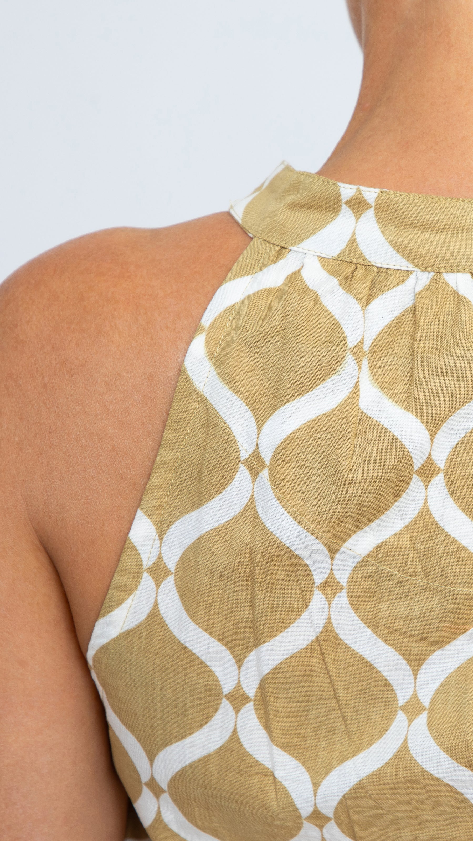 Close up of Donna Dress by Nancy The Label. Close-up of back neckline detail. Geometric Gold Trellis Print in Cotton. Maxi dress with V-neck and tiered skirt. Comes with matching belt.