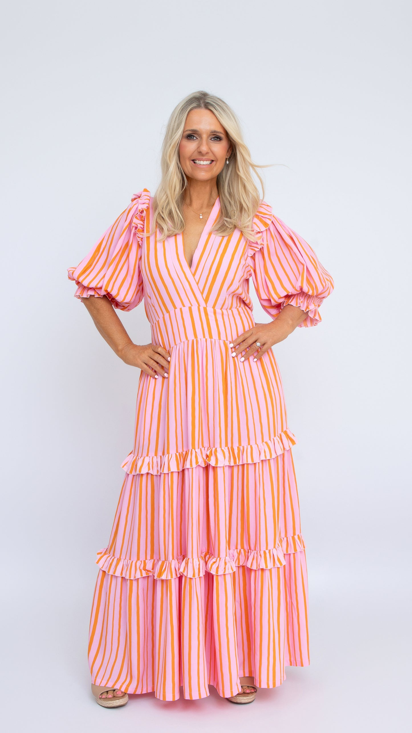 The Amy Dress in pink and orange striped rayon with V-neck and puff sleeves, full-length tiered skirt. By Nancy The Label.