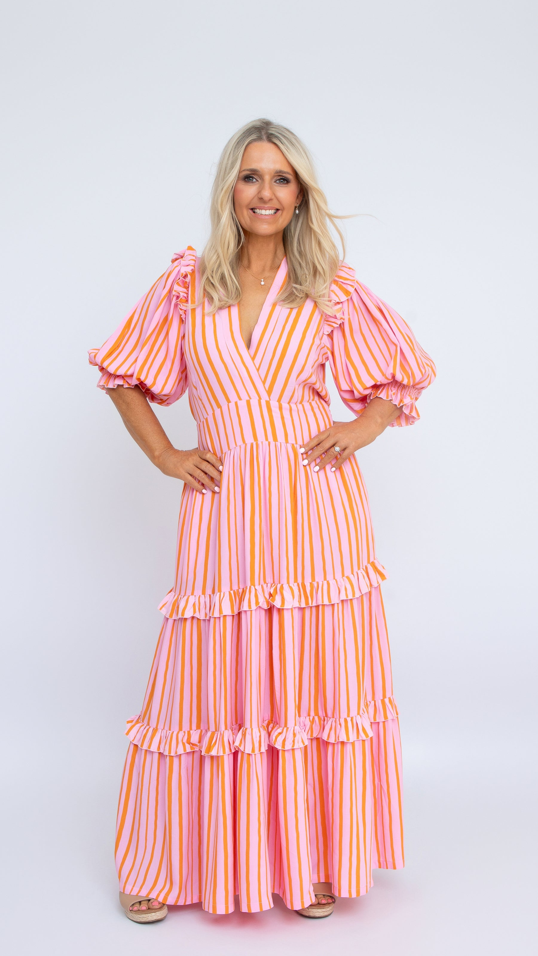 The Amy Dress in pink and orange striped rayon with V-neck and puff sleeves, full-length tiered skirt. By Nancy The Label.